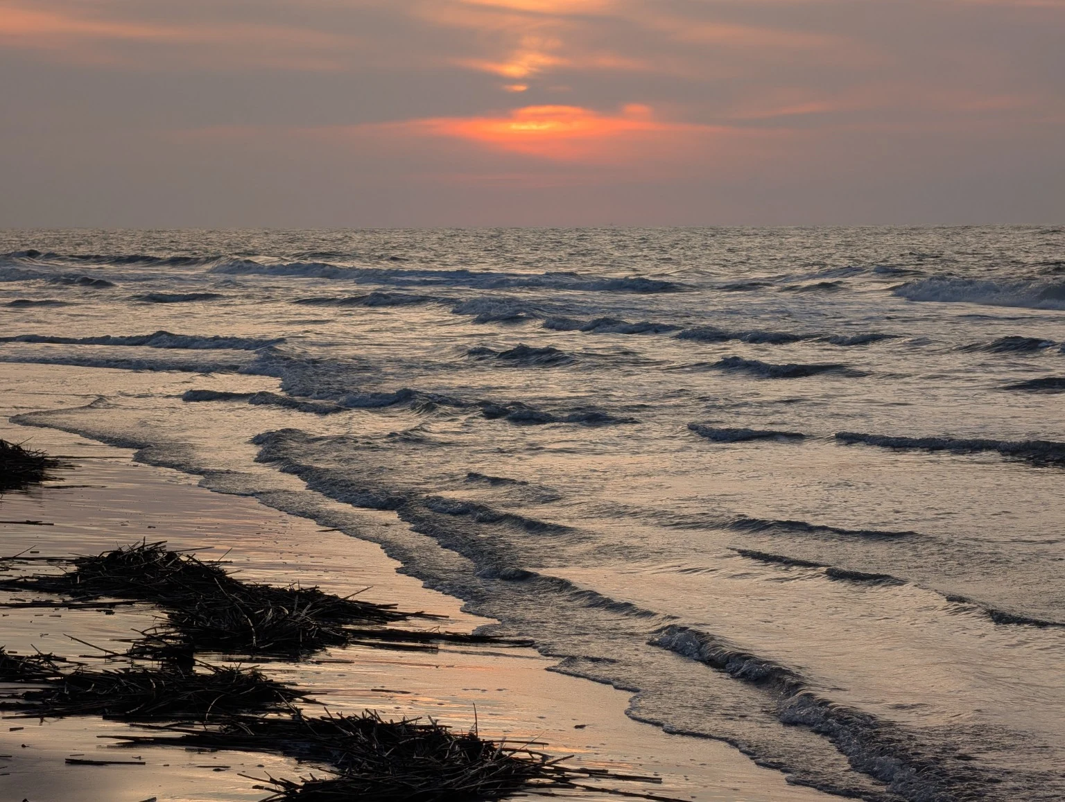 Small waves rolling onto a sandy shore under a warm orange sky. Photograph by Zachary Lund.